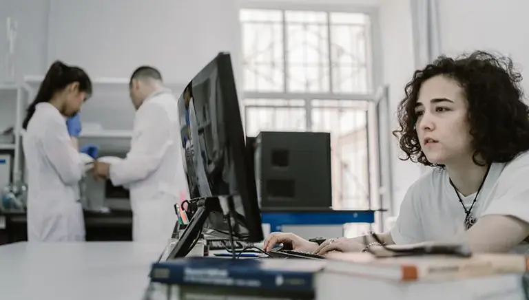 Scientist in the lab looks at a computer screen, while two others talk in the background